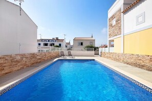 Ein Pool mit zwei Liegestühlen, umgeben von Steinmauern und Gebäuden.