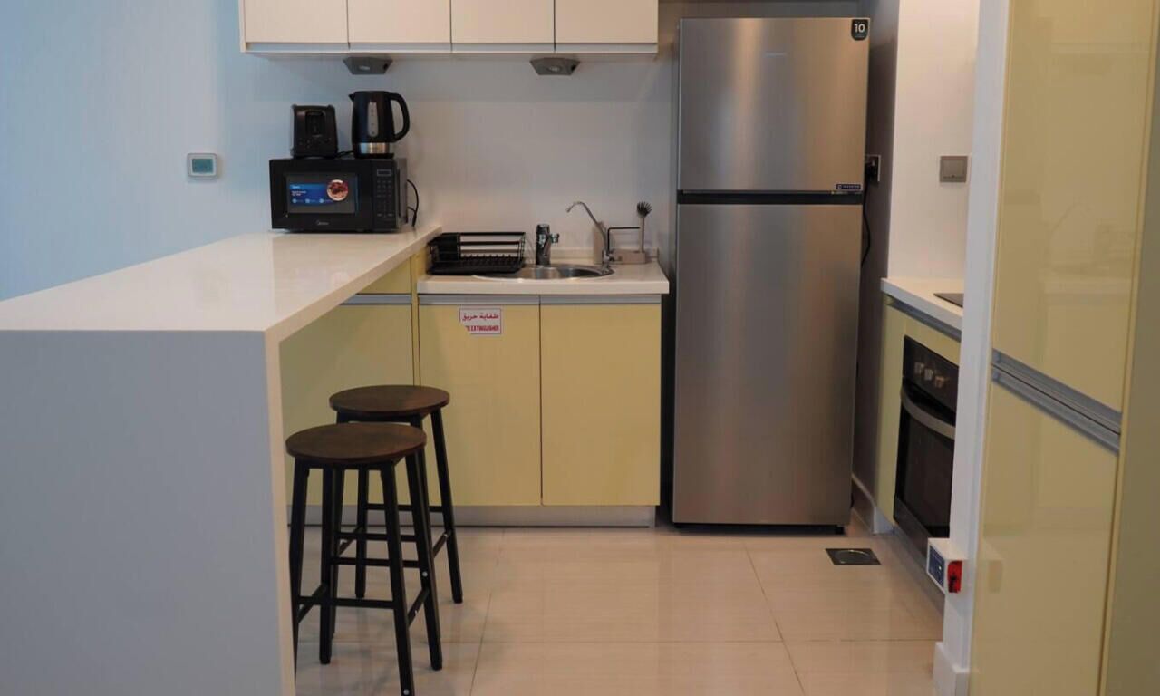 A compact kitchen with a stainless steel refrigerator, a coffee maker, and two stools.