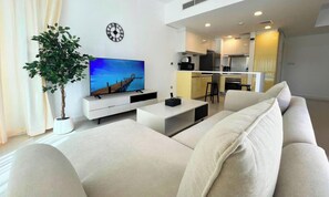 A modern living room with a sofa, a flat-screen TV, a potted plant, and a kitchen in the background. - Chic High Floor 1BR Hideaway on Reem Island (Abu Dhabi)