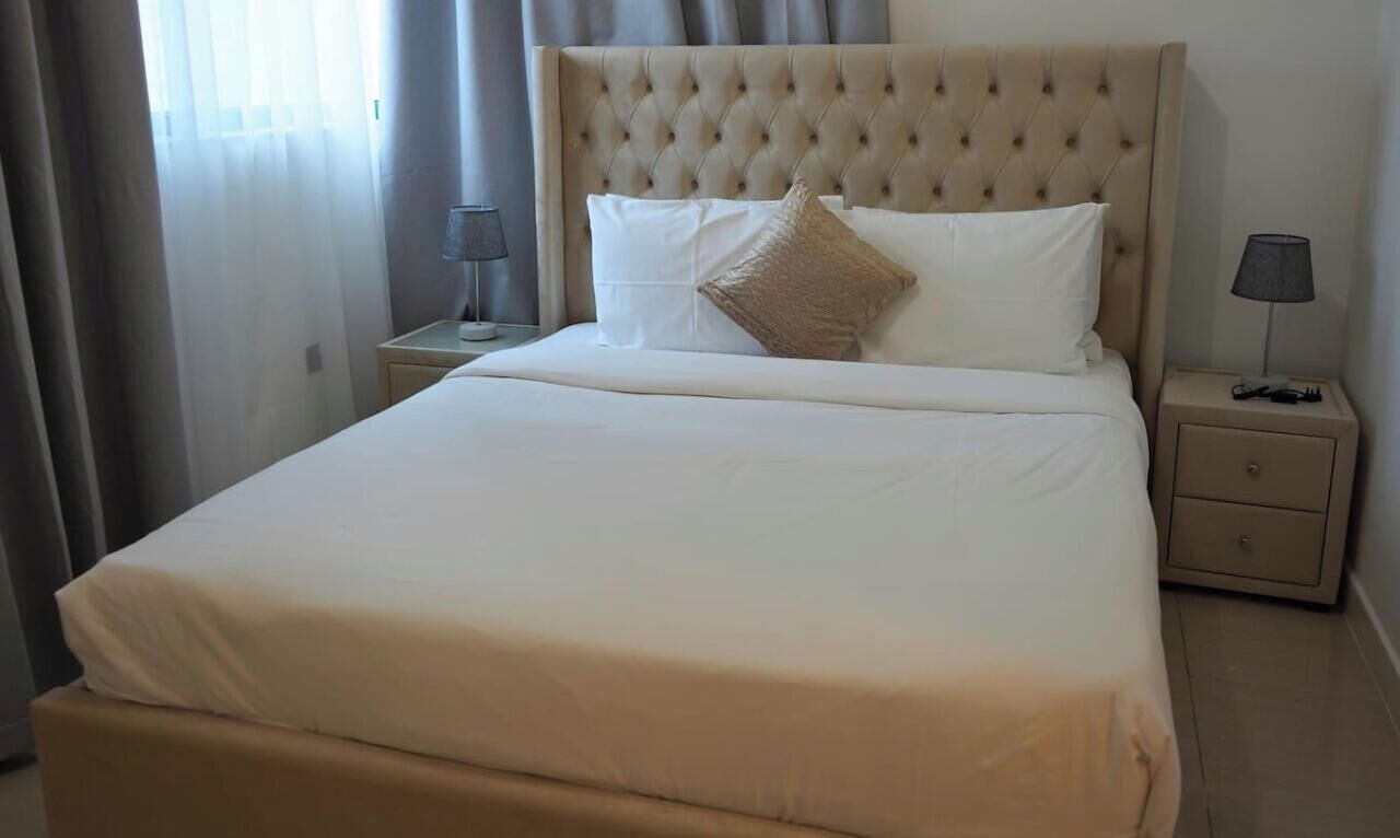 A neatly made bed with a tufted headboard, two bedside tables with lamps, and a window with curtains.