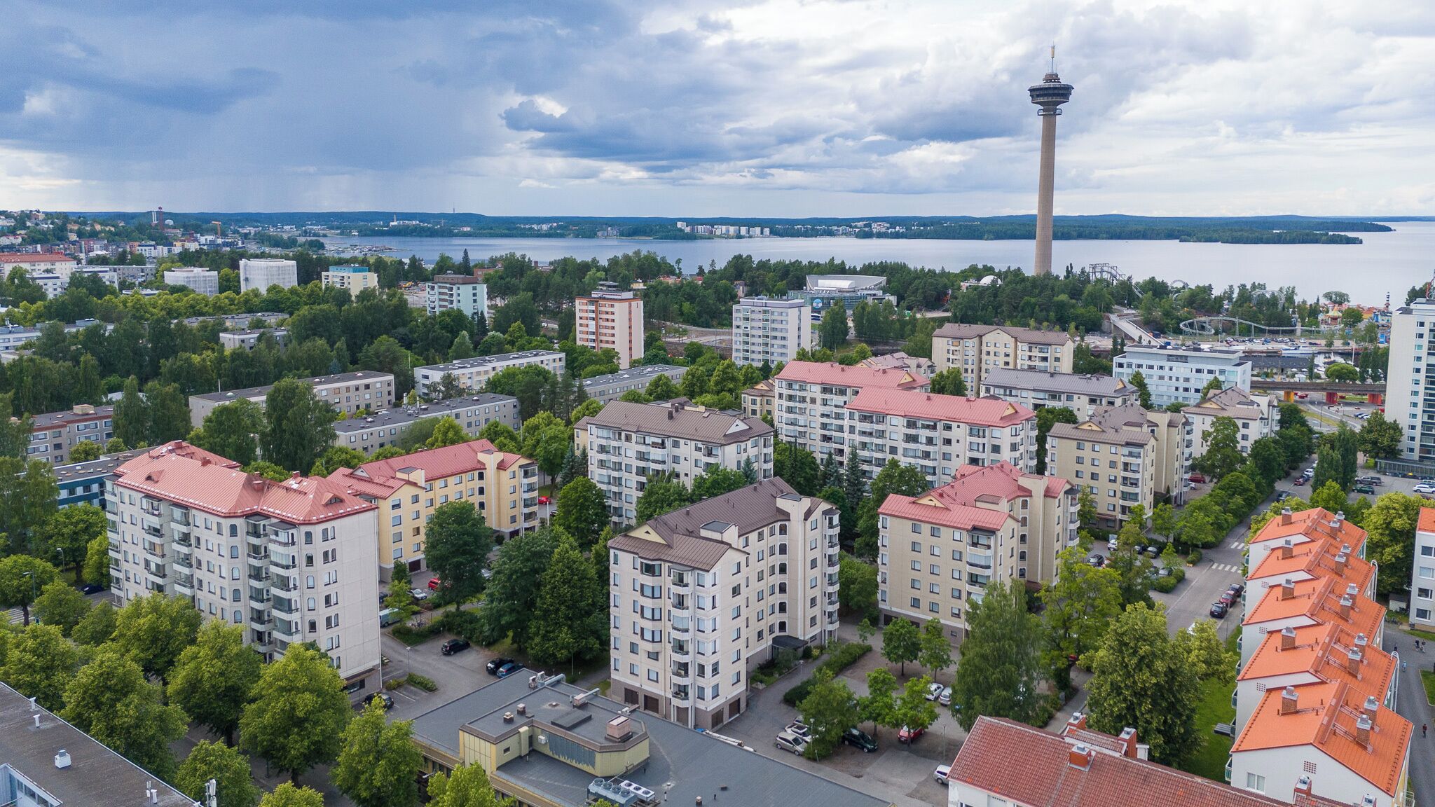 A high-rise residential building complex with multiple apartment buildings, a prominent tower, and a body of water in the background.