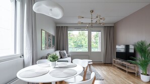 Ein modernes Wohnzimmer mit Essbereich, Fernseher und einem großen Fenster mit Vorhängen.