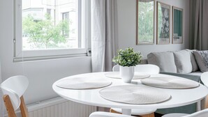 Ein modernes Wohnzimmer mit einem runden Tisch, weißen Stühlen, einer Zimmerpflanze und einem Sofa.