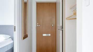 Een hal met een houten deur, een bed met een witte matras, een hangend spiegel en een lamp.