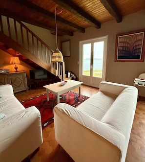 Ein Wohnzimmer mit Treppe, einem weißen Sofa, einem kleinen Tisch und Meerblick durch eine Tür.