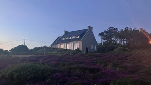 Et hus med skråt tag, omgivet af lilla lyng.