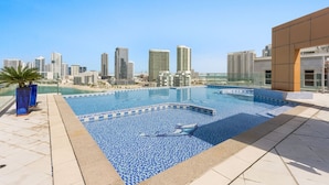 Ein Pool auf dem Dach mit Blick auf eine Stadtlandschaft, umgeben von Gebäuden und einer Palme.