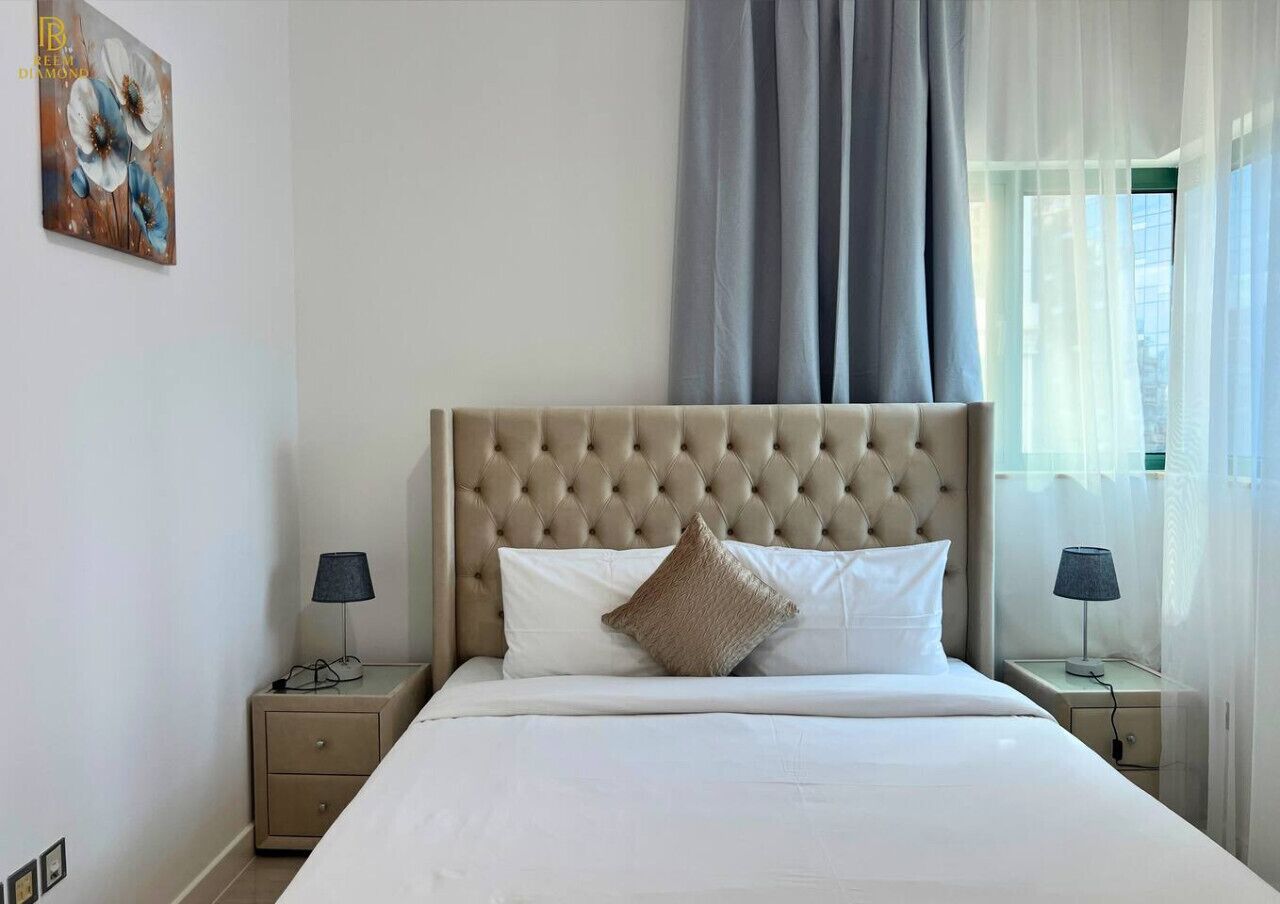 A neatly made bed with a tufted headboard, two bedside tables with lamps, and a painting on the wall.