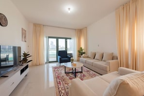 Una sala de estar moderna con sofá, sillón, mesa de centro, televisor y vistas a la ciudad a través de amplios ventanales.