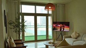 Ein Wohnzimmer mit großem Fenster, Fernseher, Sofa, Sessel und einer Pflanze.