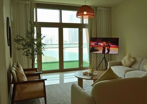 Una sala de estar con un ventanal grande, televisor, sofá, sillón y una planta.