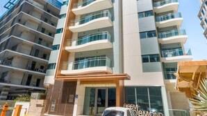Ein mehrstöckiges Hotel mit modernem Design, mit Balkonen auf jeder Etage, einem zentralen Eingang und einem davor stehenden Auto.