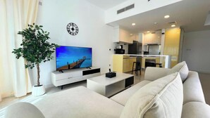 Ein modernes Wohnzimmer mit einer Couch, einem Fernseher, einer Pflanze und einer Küche im Hintergrund.