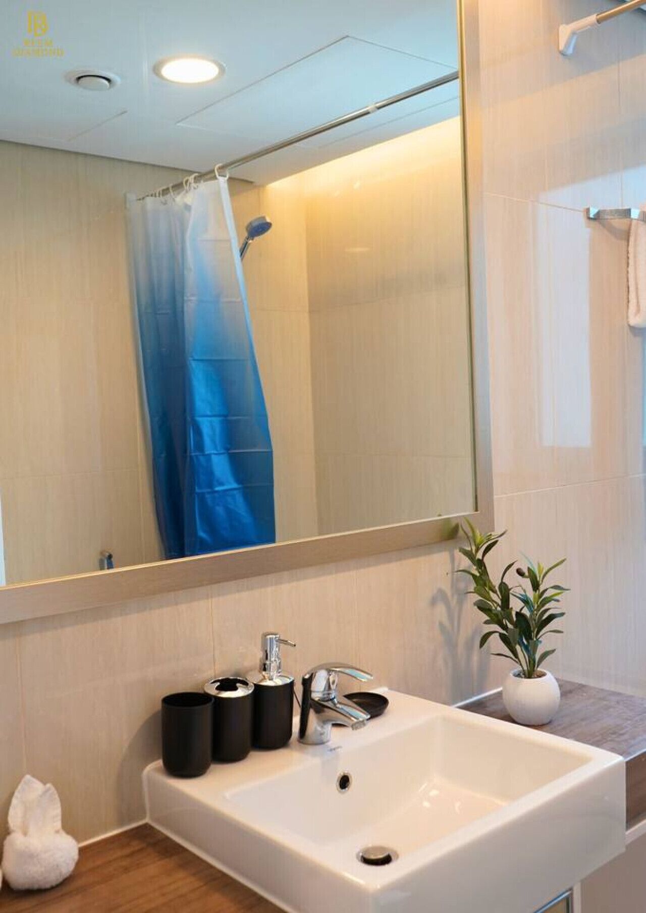 A bathroom with a white sink, a mirror, a shower curtain, a towel rack, and a potted plant.