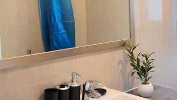 A bathroom with a white sink, a mirror, a shower curtain, a towel rack, and a potted plant.