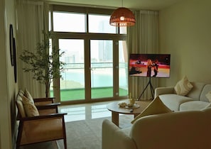 Ein Wohnzimmer mit großem Fenster, Fernseher, Sofa, Sessel und einer Pflanze.