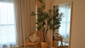 A room with a wicker chair, a potted plant, a mirror, and a patterned rug. - Beach View 3BR Duplex Retreat in Al Reem (Abu Dhabi)