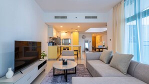 A modern living room with a flat-screen TV, sofa, coffee table, and dining area. - Luxury 1BR with Gulf Views (Abu Dhabi)