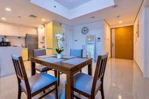 A modern kitchen with a dining area, a clock on the wall, and a door leading to another room. - Luxury 1BR with Gulf Views (Abu Dhabi)