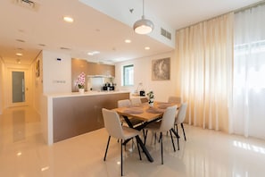 A modern kitchen with a central island, a dining area with a table and chairs, and a large window with curtains. - Lavish 2BR Apt next to beach (Abu Dhabi)