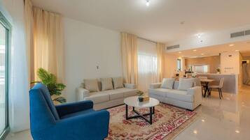 A modern living room with two sofas, a blue armchair, a coffee table, and a dining area with a table and chairs.