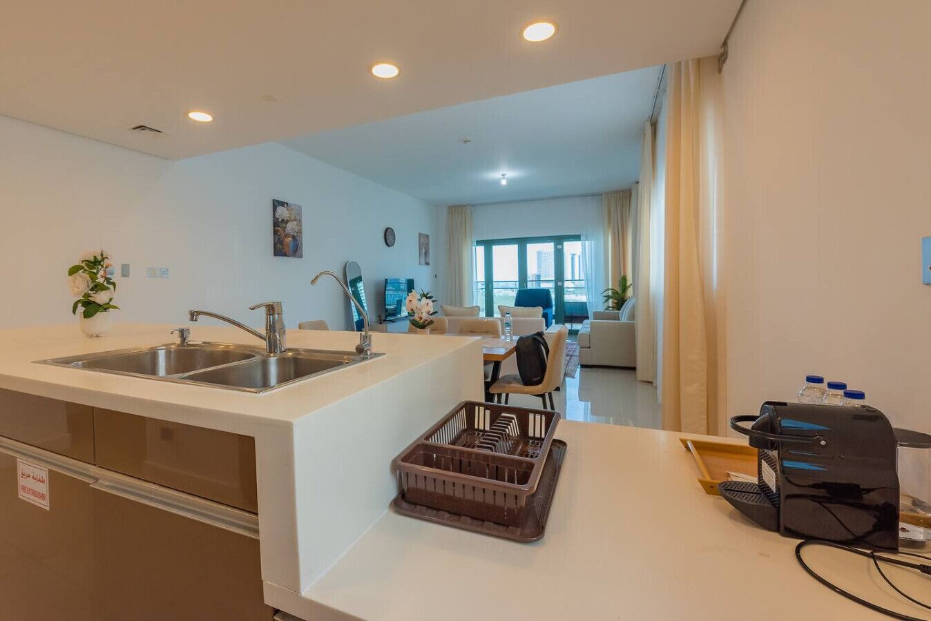 A modern kitchen with a sink, a dining area with a table and chairs, and a living room with a sofa and a TV.
