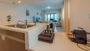 A modern kitchen with a sink, a dining area with a table and chairs, and a living room with a sofa and a TV. - Stylish Apt with Balcony & Views (Abu Dhabi)