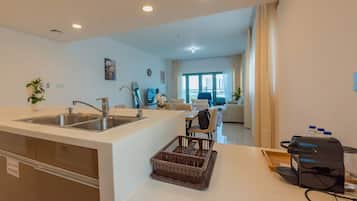 A modern kitchen with a sink, a dining area with a table and chairs, and a living room with a sofa and a TV.