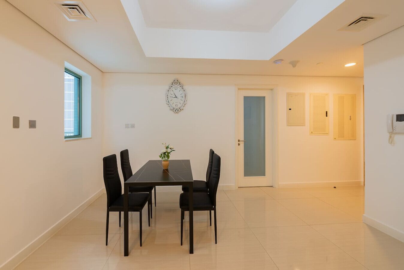 A modern dining area with a table and chairs, a decorative wall clock, and a door leading to another room.