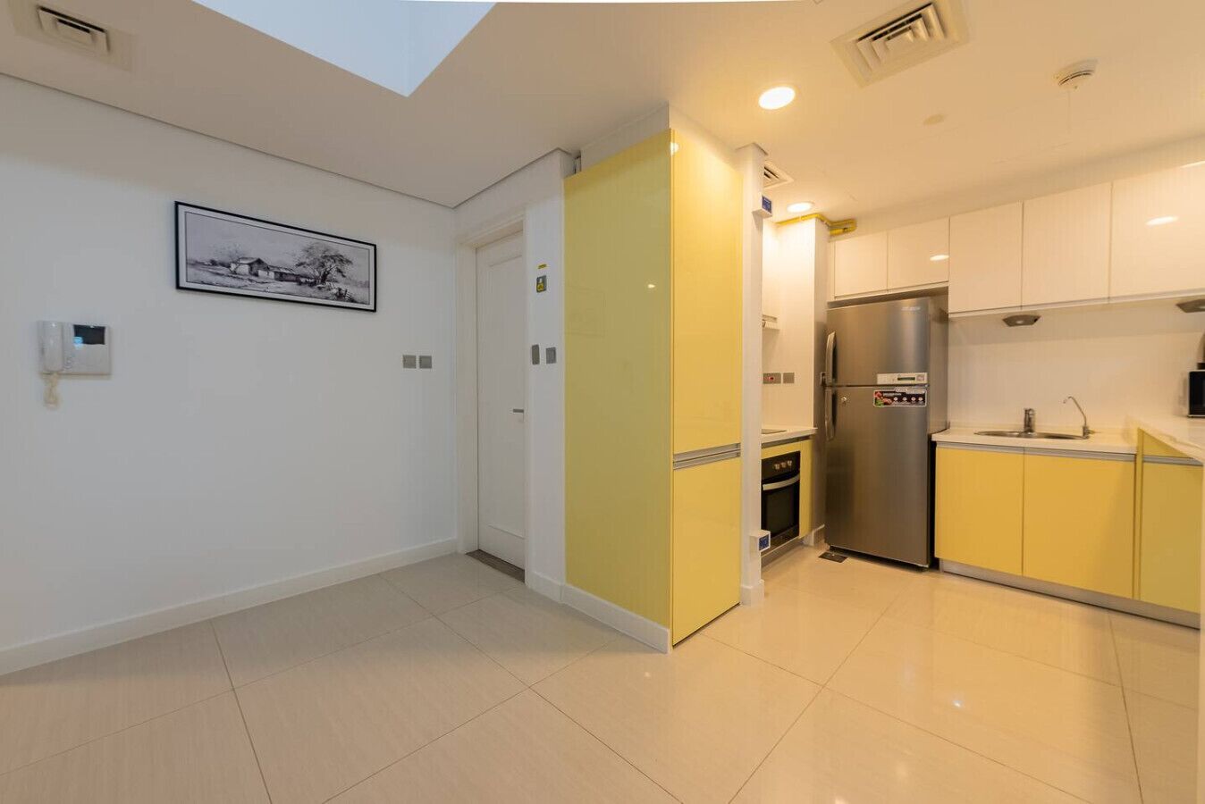 A modern kitchen with a built-in oven, a stainless steel refrigerator, and a yellow accent wall.