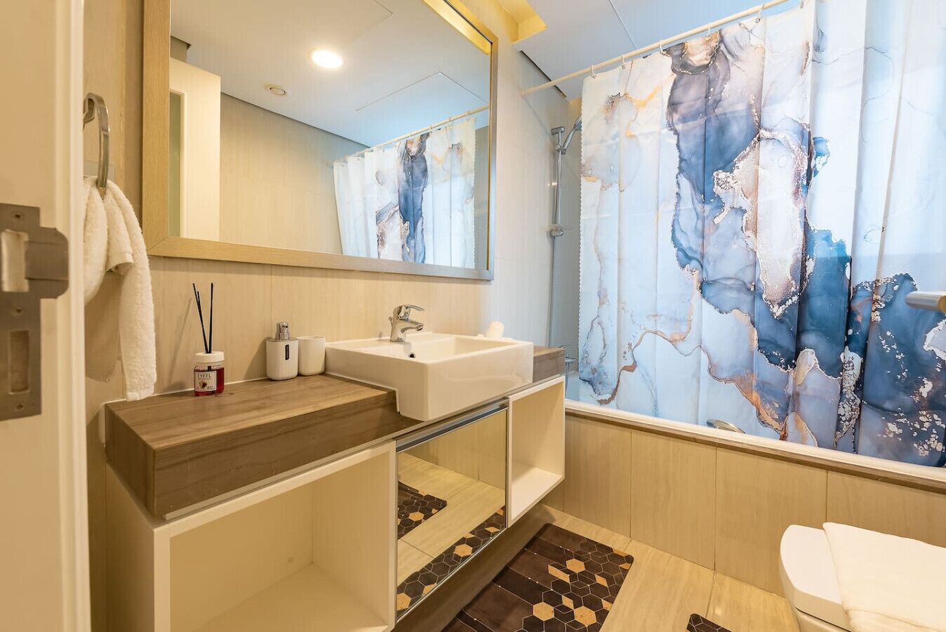 Une salle de bain moderne avec un meuble-lavabo en bois, un lavabo blanc, un miroir et un rideau de douche à motif marbré.