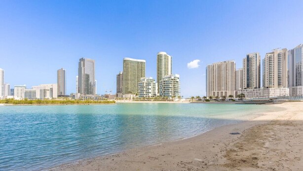 Un paysage urbain côtier avec de hauts immeubles, une plage de sable et des eaux calmes.