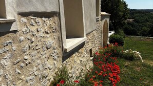 Un edificio in pietra con un'ampia porta aperta, una piccola finestra e un'aiuola con fiori rossi.