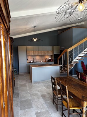 A modern kitchen with a central island, wooden dining table, and chairs, a staircase, and a hanging light fixture. - Authentic, fully renovated farmhouse in the heart of nature, absolute peace and quiet (Sault)