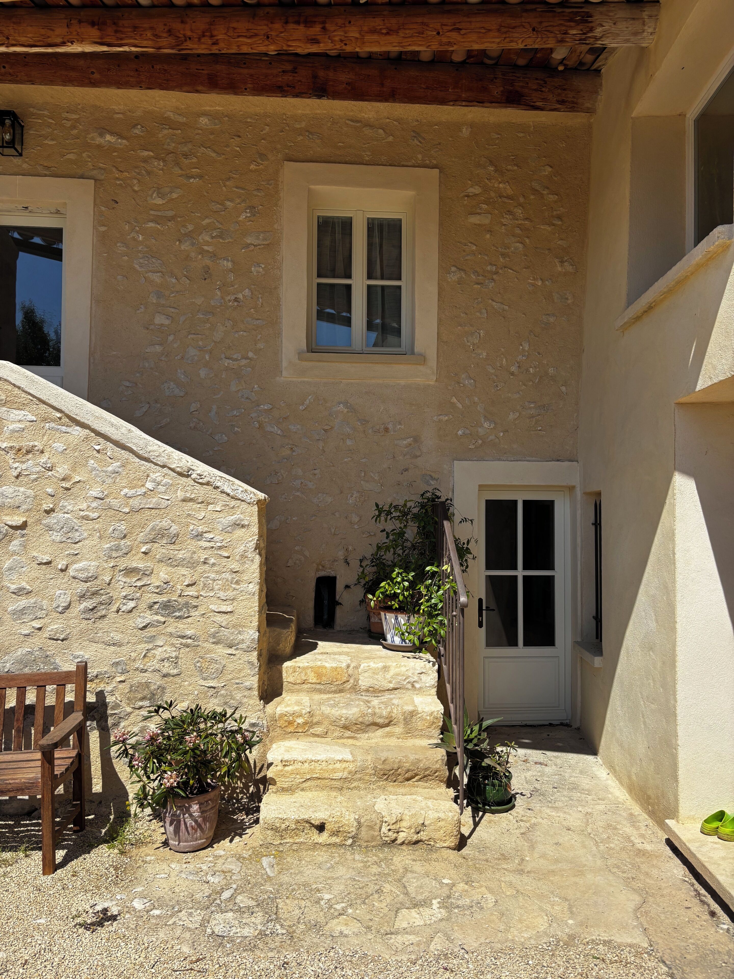 Un escalier en pierre mène à une porte, avec un banc et des plantes en pot sur le côté gauche.