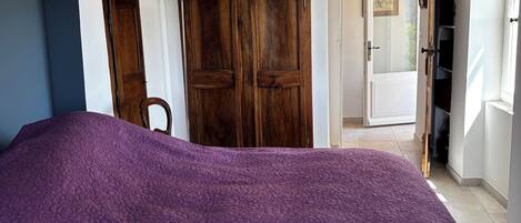 A bedroom with a purple floral bedspread, wooden wardrobe, and a white ceiling.