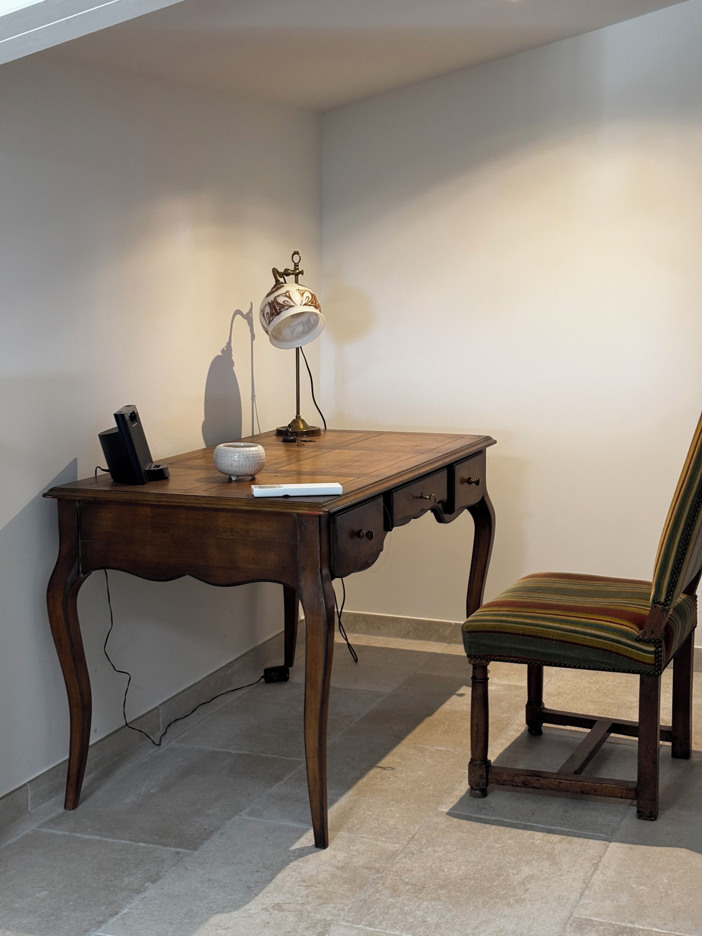 A wooden desk with a lamp, a chair, and a smartphone on it.