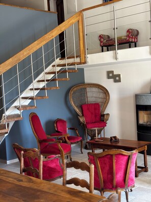 A staircase with wooden railings, a blue wall, and a seating area with red upholstered chairs and a wicker chair. - Authentic, fully renovated farmhouse in the heart of nature, absolute peace and quiet (Sault)