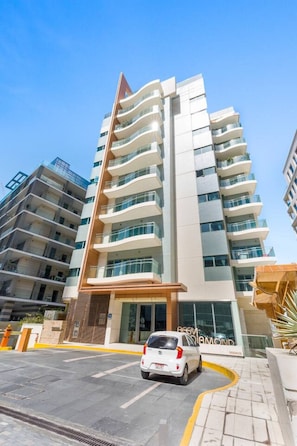 A multi-story hotel with a modern design, featuring balconies on each floor, a central entrance, and a car parked in front. - Stylish 2BR Apt Next to the Beach (Abu Dhabi)
