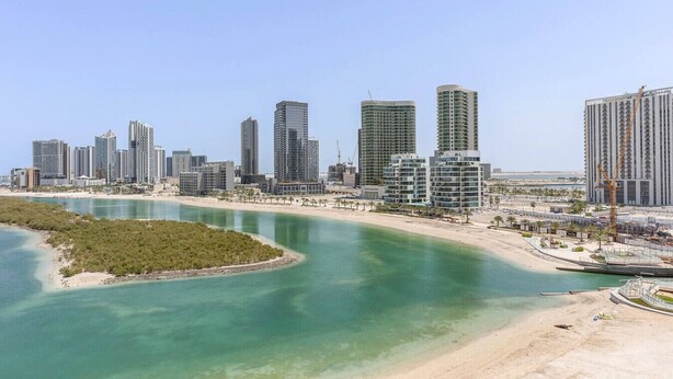 Un paysage urbain côtier avec des immeubles modernes de grande hauteur, un ciel bleu dégagé et une rivière qui serpente à travers le paysage.