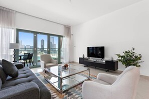 Un salon moderne comprenant un canapé, un fauteuil, une table basse, un téléviseur et un balcon avec vue sur la ville.