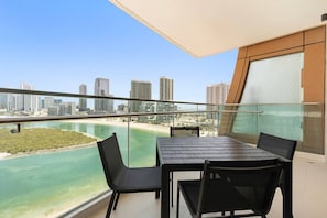 A balcony with a table and chairs overlooking a beach and city skyline. - Fully Equipped 2BR Apartment near to the Beach (Abu Dhabi)