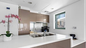Une cuisine moderne dotée d’appareils électroménagers en acier inoxydable, d’un plan de travail blanc et d’une fenêtre avec des stores.