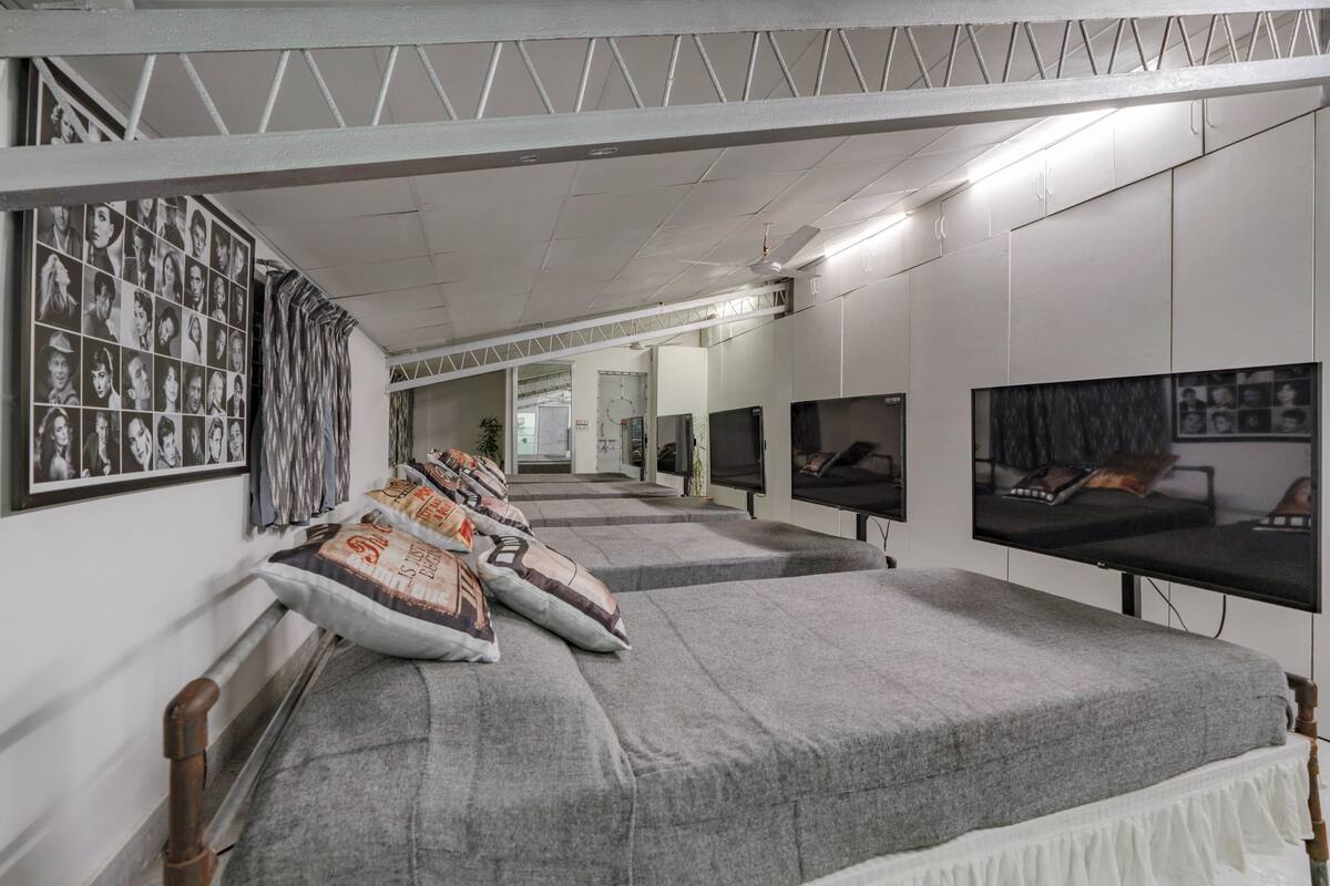 A room with a long bed, multiple televisions, and a wall with photographs.