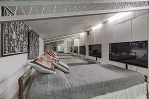 A room with a long bed, multiple televisions, and a wall with photographs.