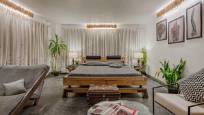 A bedroom with a wooden bed, two nightstands, a grey sofa, a small table, and a suitcase.