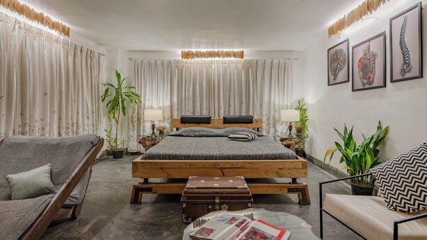 Un dormitorio con una cama de madera, dos mesitas de noche, un sofá gris, una pequeña mesa y una maleta.