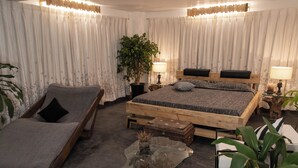 Un dormitorio con cama, una chaise longue, una mesita de vidrio y una planta en maceta.