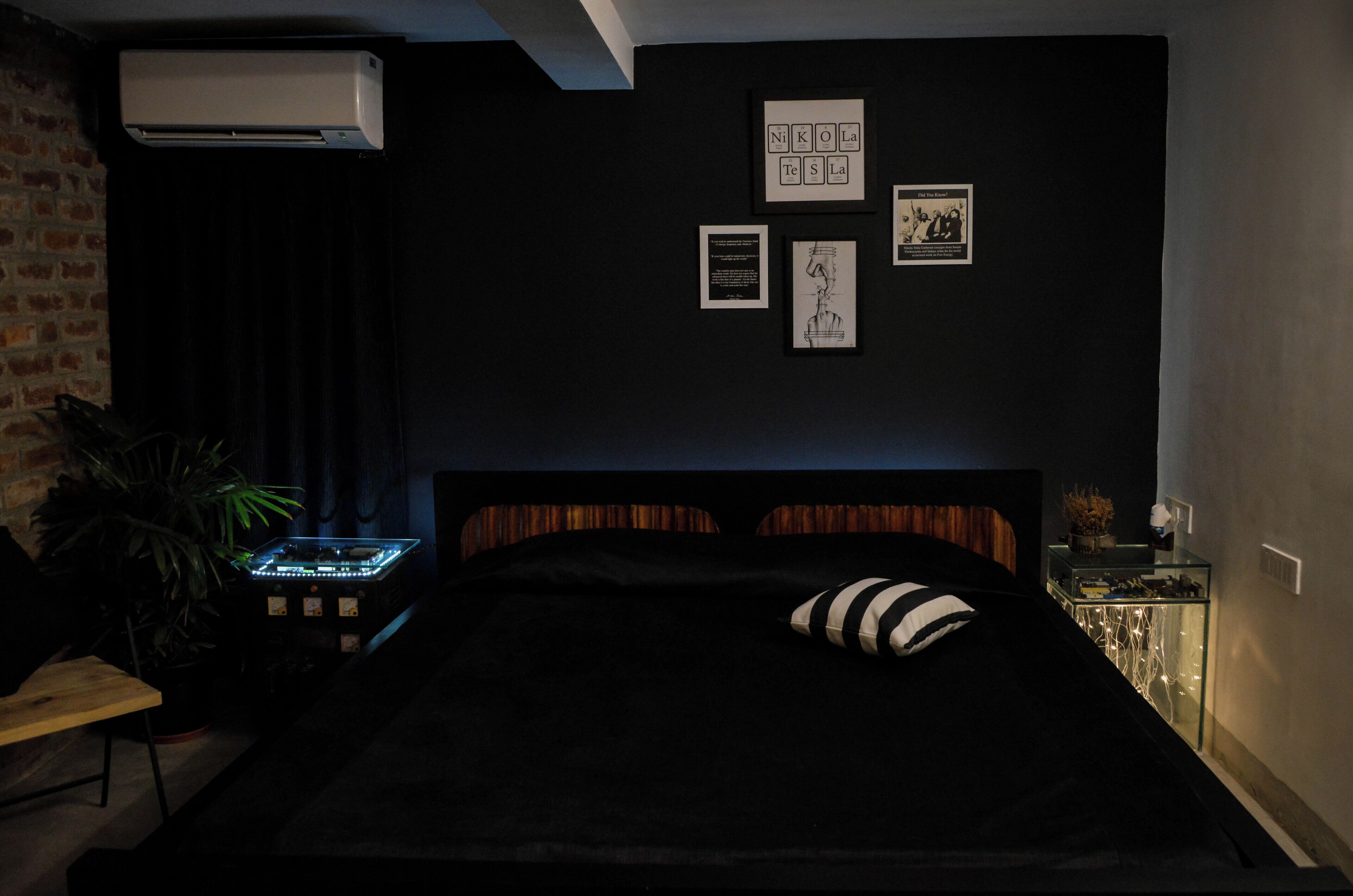A dark-themed bedroom with a bed, a wall-mounted air conditioner, and framed artwork.