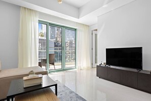 Una sala de estar moderna con un sofá, una mesa de centro, un televisor sobre un mueble bajo y un ventanal corredero que da a un balcón exterior.